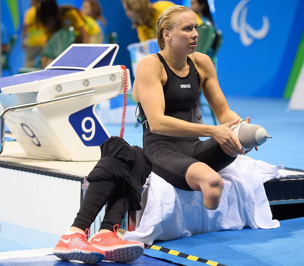 Jessica Long sitting beside pool putting on her prosthetic legs