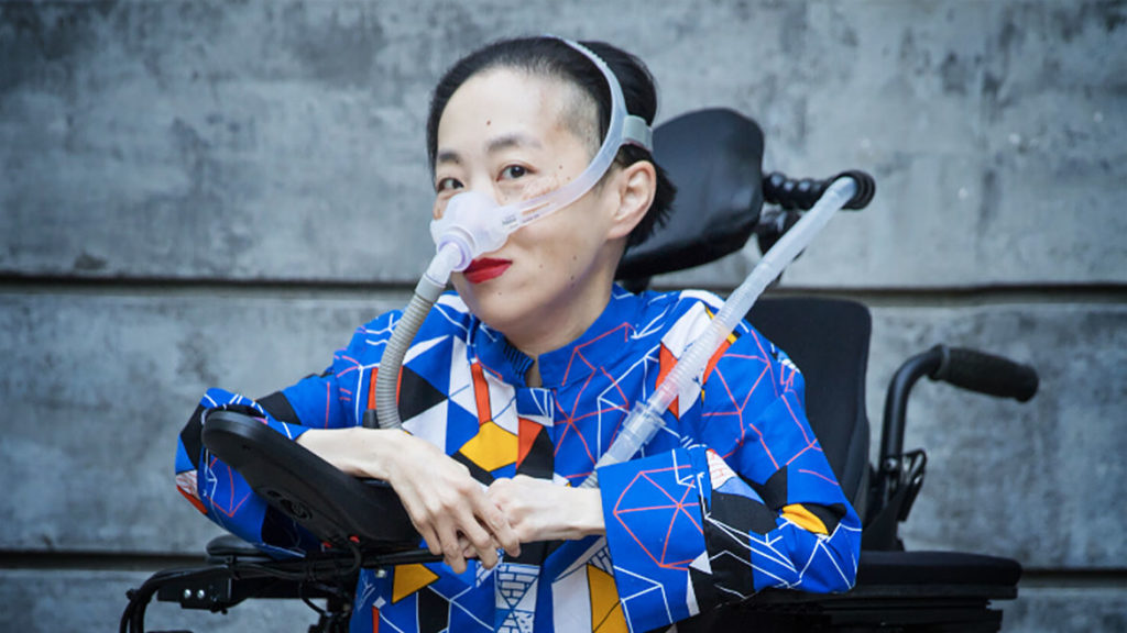 Asian American woman in a wheelchair who wears a mask over her nose with a tube for her BiPAP machine.