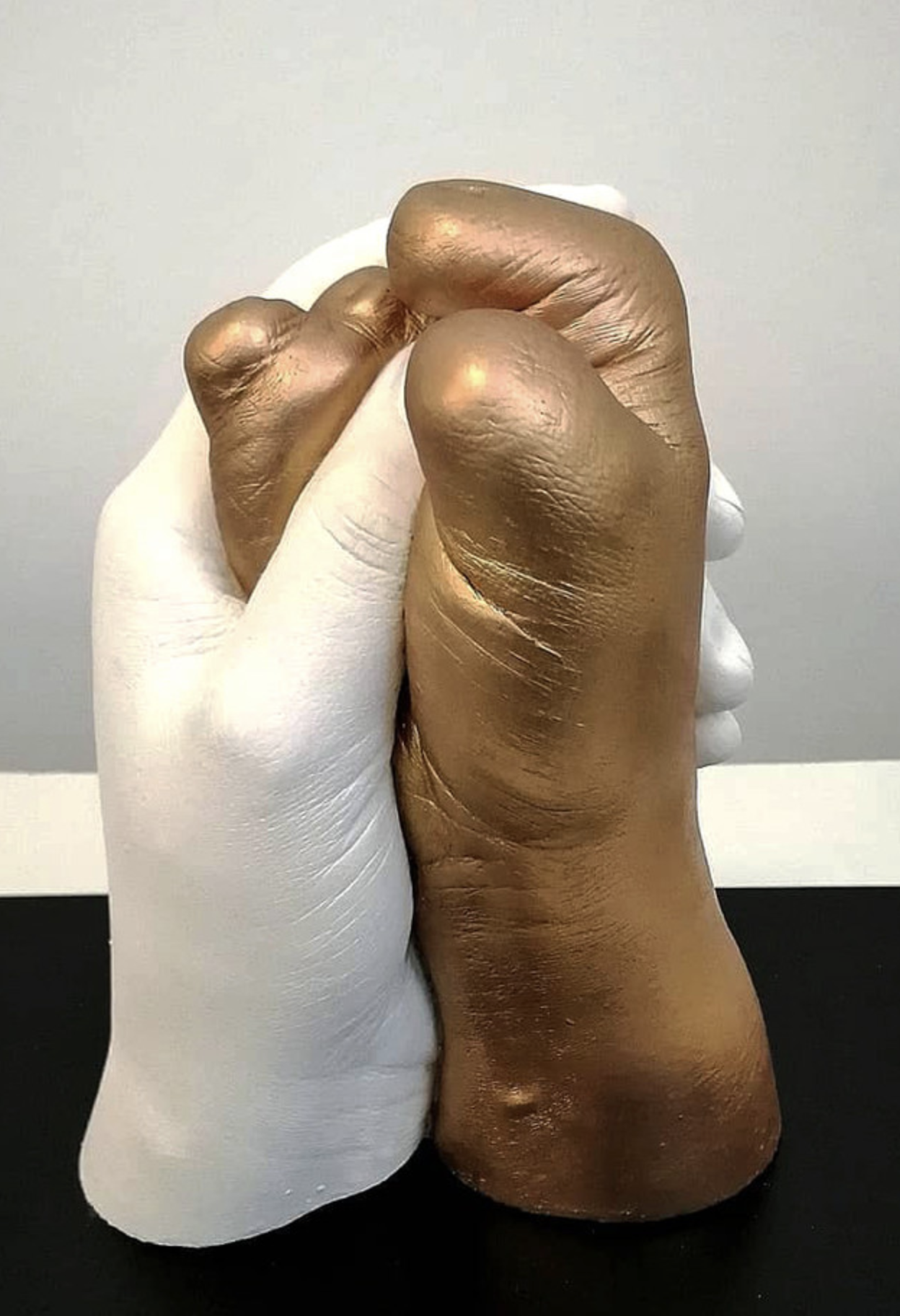 sculpture of two hands intertwined, one white and one gold with missing fingers and thumb