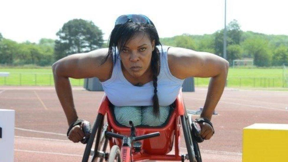 black woman wearing light coloured tee shirt racing redcolored wheelchair