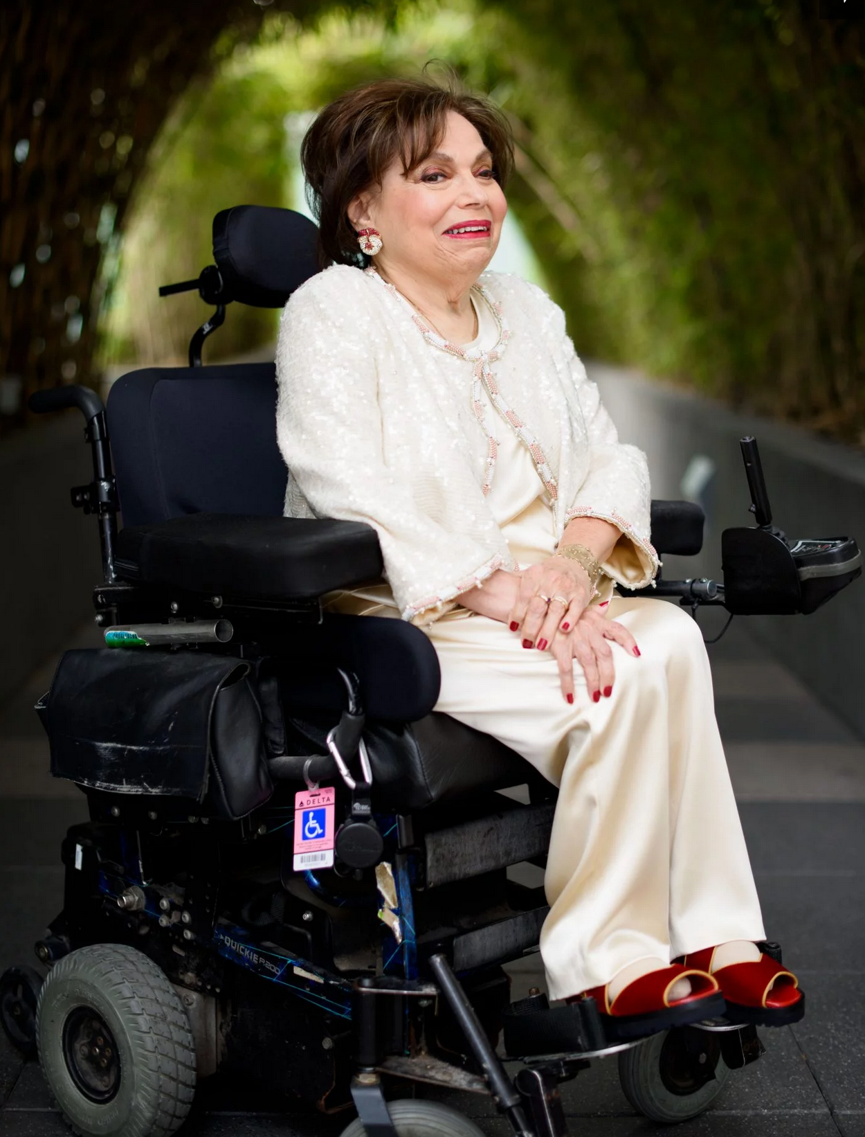 Judy Heumann wearing champagne silk pantsuit sitting in her wheelchair