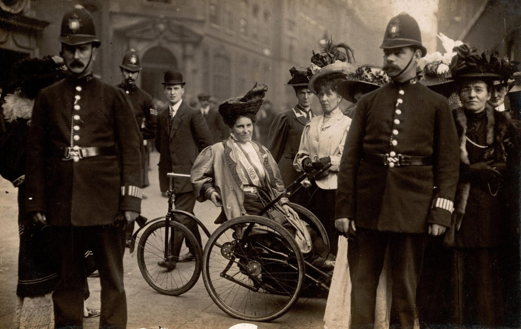 May Billinghurst sitting in her modified tricycle surrounded by policemen